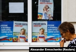 Женщина идет мимо плакатов с цитатой президента России Владимира Путина: «Русские и украинцы — один народ, единое целое». Херсон, 25 июля 2022 года