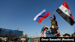 Сирийцы размахивают сирийскими и российскими флагами, протестуя против ракетных ударов США и их союзников. Дамаск, 14 апреля 2018 года.
