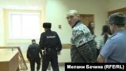 Блогера Вадима Тюменцева ведут в зал суда, где его судят за публикацию видеоролика в Интернете, в котором он критикует военное вмешательство России в Украине.